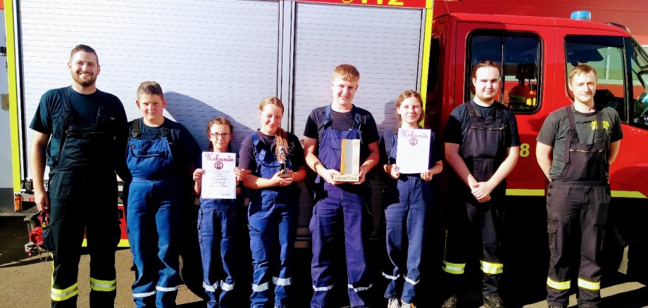 7 Jugendliche der Jugendfeuerwehr stehen mit Ihrem Betreuer vor einem Feuerwehrfahrzeug. Einige halten Urkunden in der Hand.