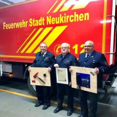 Klaus Lukes, Wolfgang Hertel, Klaus Hartmann stehen vor einem Fahrzeug der Feuerwehr Neukirchen und halten Ihre Auszeichnungen in den Händen.